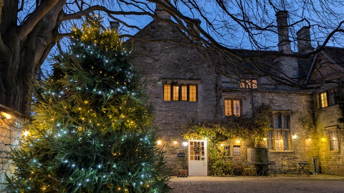 Grantham House at Christmas with golden lights strung along its façade and a huge Christmas tree with blue and gold lights to the left in the courtyard.
